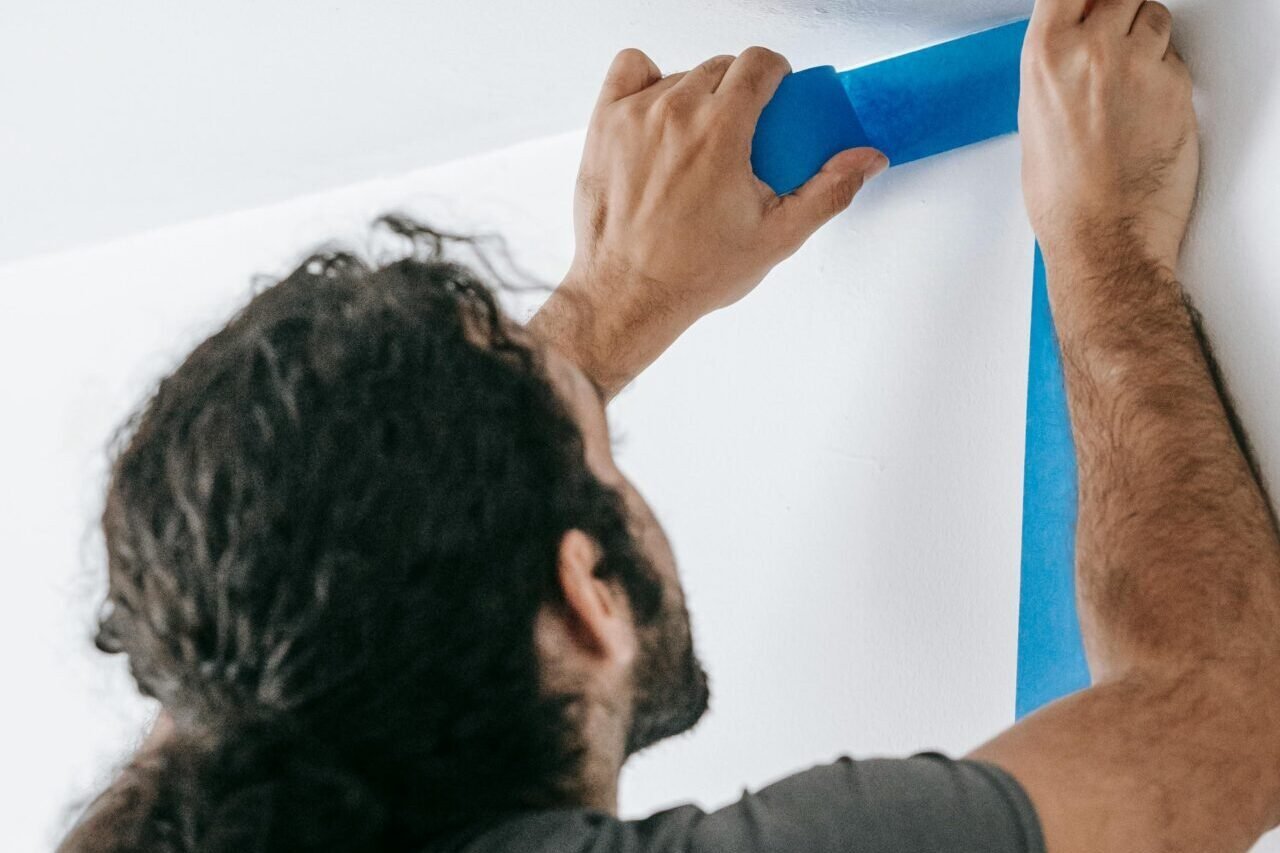 A man applying blue tape on a wall during a home renovation project, showcasing painting preparation.